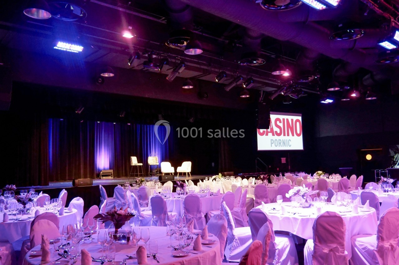 Salle de réception avec tables dressées, éclairage coloré et scène en arrière-plan portant l'inscription ’Casino Pornic’.