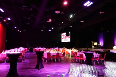 Bâtiment moderne en bord de rivière, entouré de verdure, avec un pont piétonnier au premier plan.