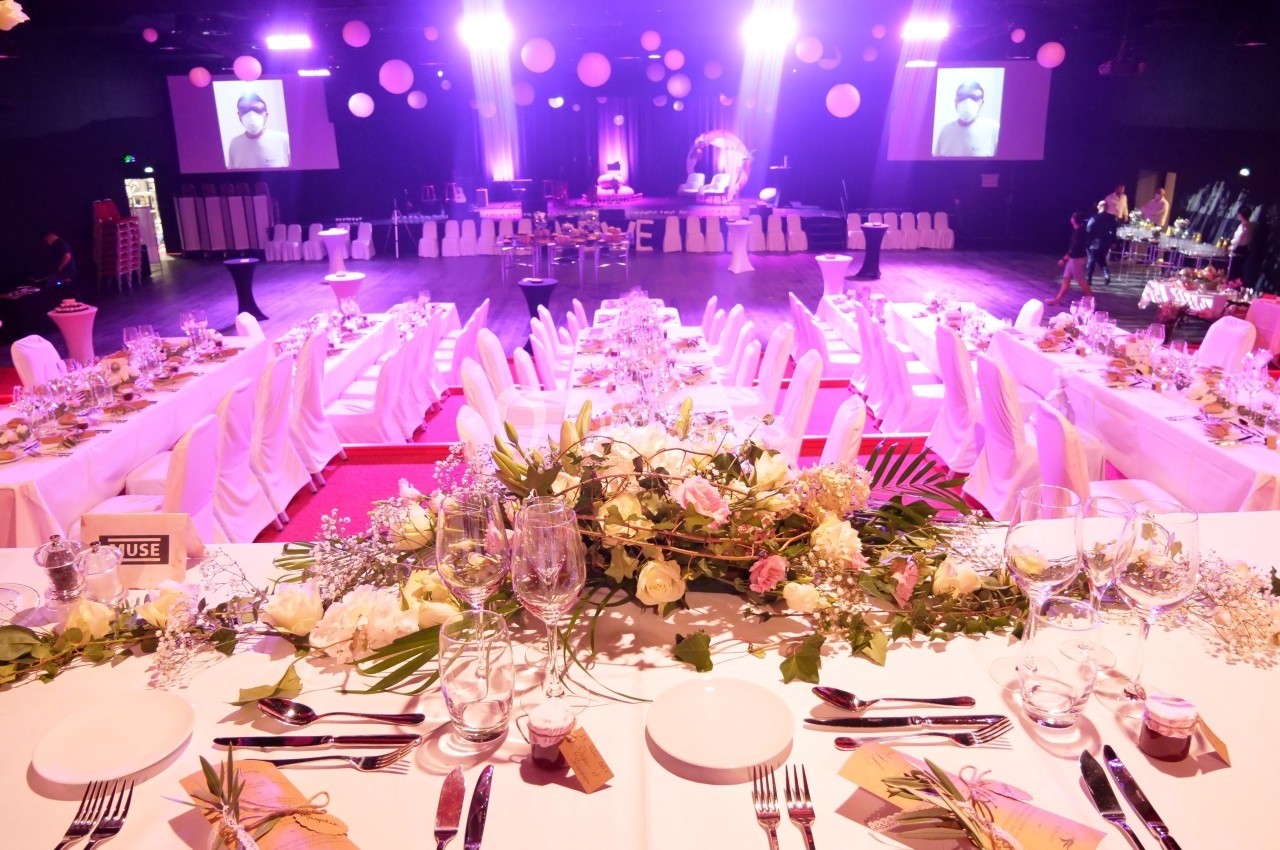 Salle de réception décorée pour un événement, avec tables dressées, éclairage rose et ambiance festive.