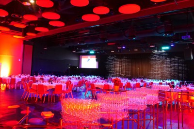 Bâtiment moderne en bord de rivière, entouré de verdure, avec un pont piétonnier au premier plan.