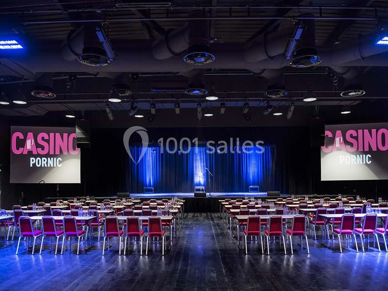 Salle de spectacle avec des rangées de chaises rouges, une scène éclairée en bleu et des écrans affichant ’Casino Pornic’.