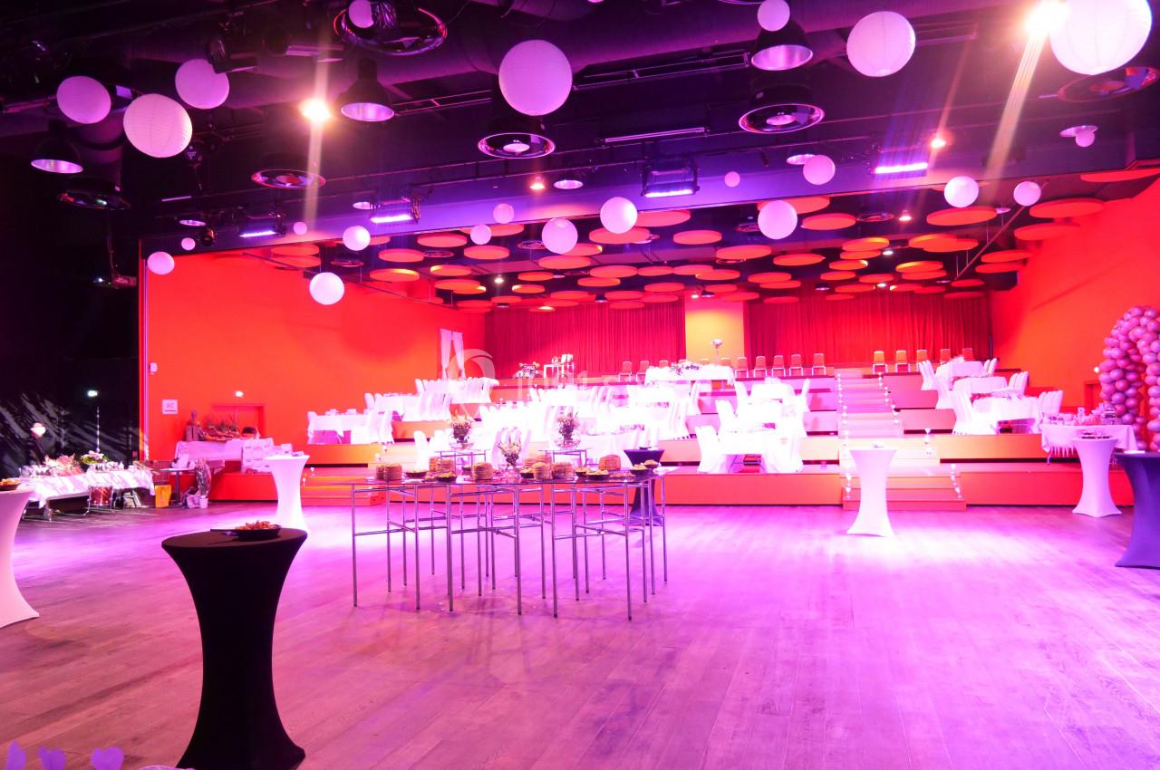 Salle de réception lumineuse avec tables dressées, décorations suspendues et éclairage rose.