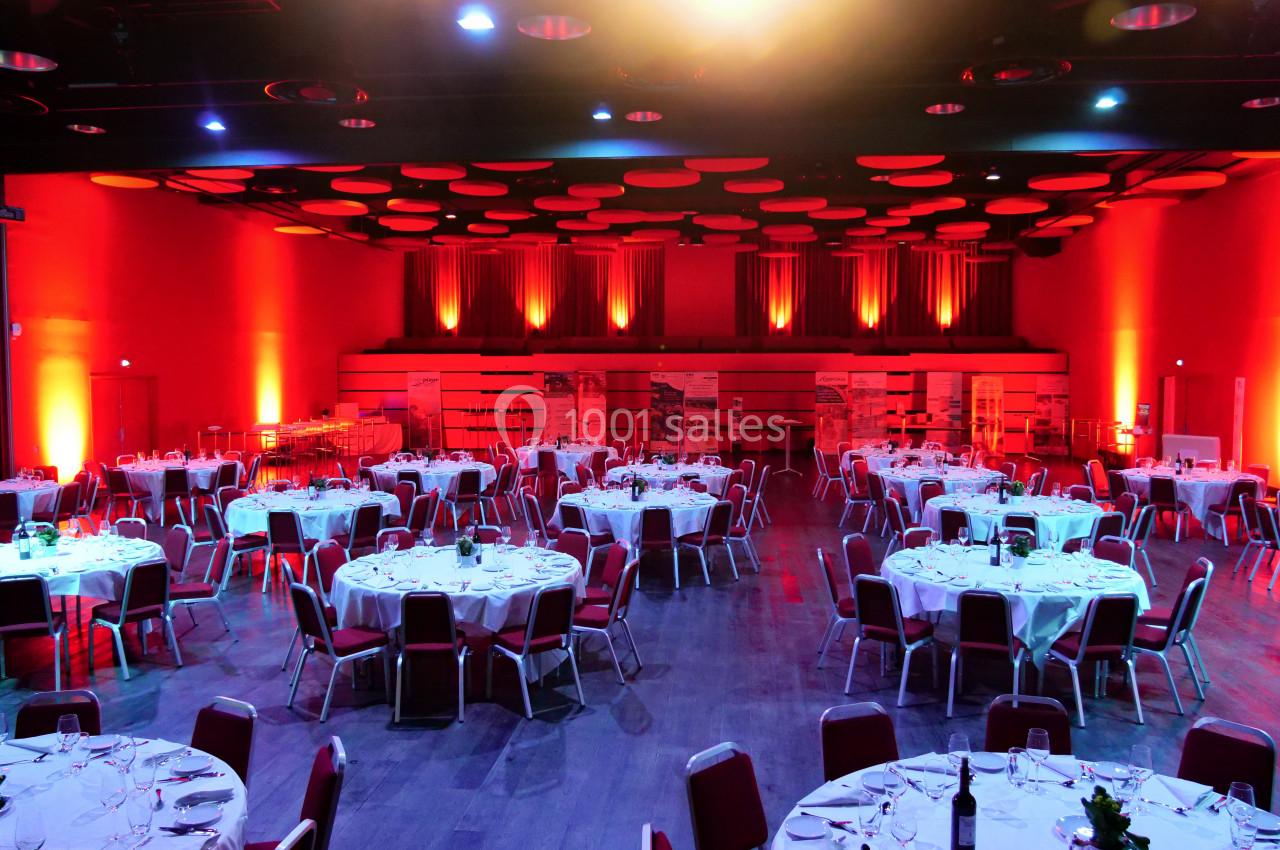 Salle de réception avec tables rondes dressées, éclairée par des lumières rouges et un plafond décoratif.