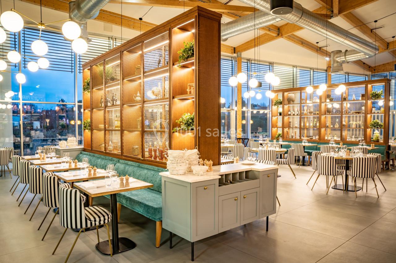 Salle de restaurant lumineuse avec mobilier moderne, banquettes turquoise, chaises rayées et étagères décoratives en bois.