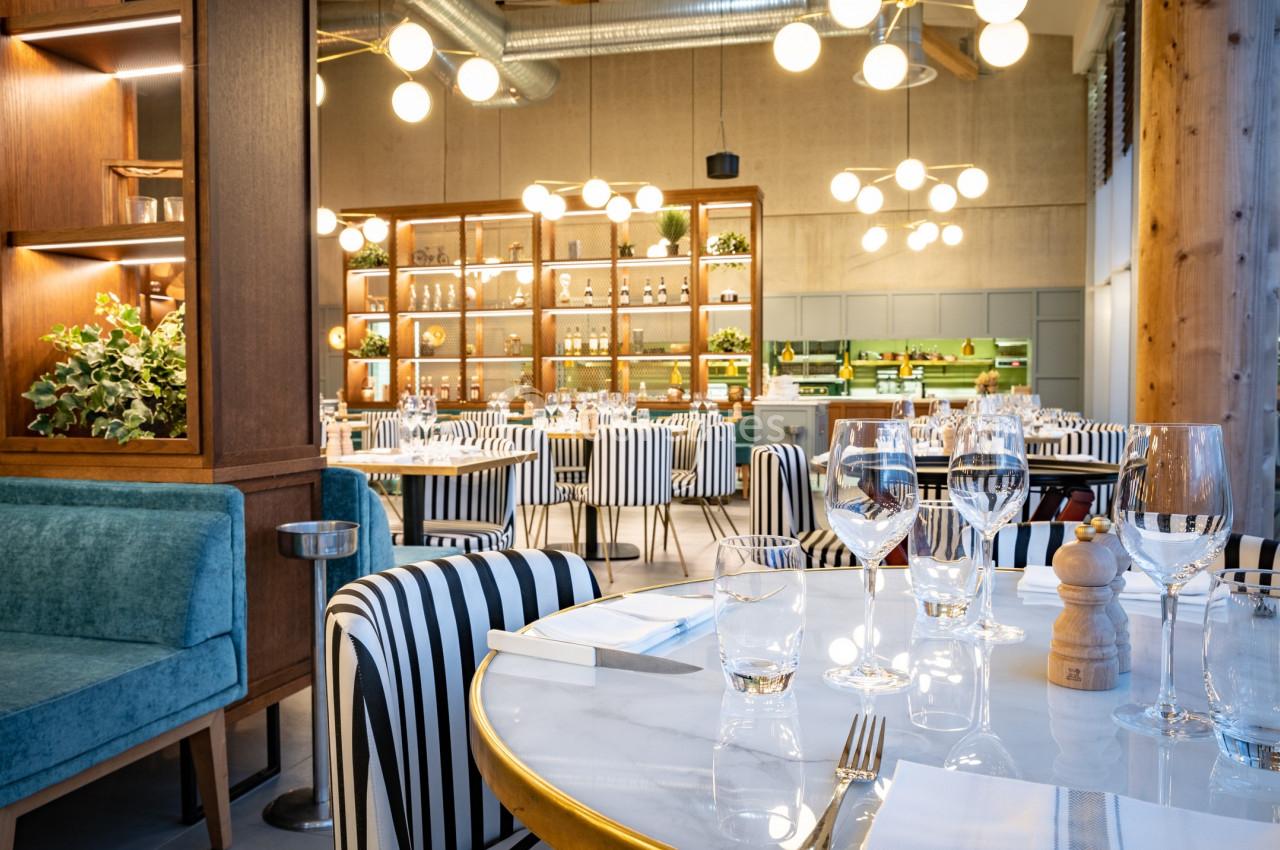 Salle de restaurant moderne avec tables dressées, chaises à rayures, étagères décoratives et éclairage suspendu.