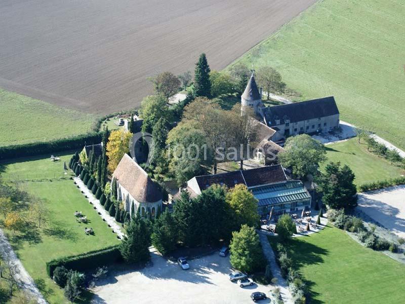 Vue aérienne d'un domaine rural avec une église, des bâtiments anciens et des espaces verts entourés de champs.