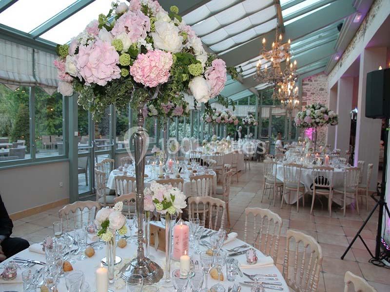 Salle de réception lumineuse avec tables décorées de centres de table fleuris et chandeliers élégants.
