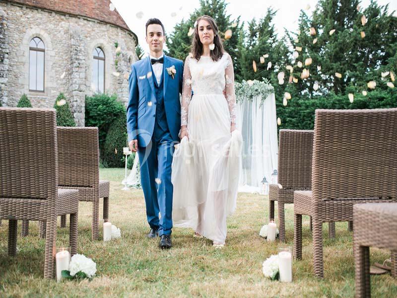 Un couple en tenue de mariage marche dans une allée extérieure décorée, entourée de chaises et de pétales de fleurs.
