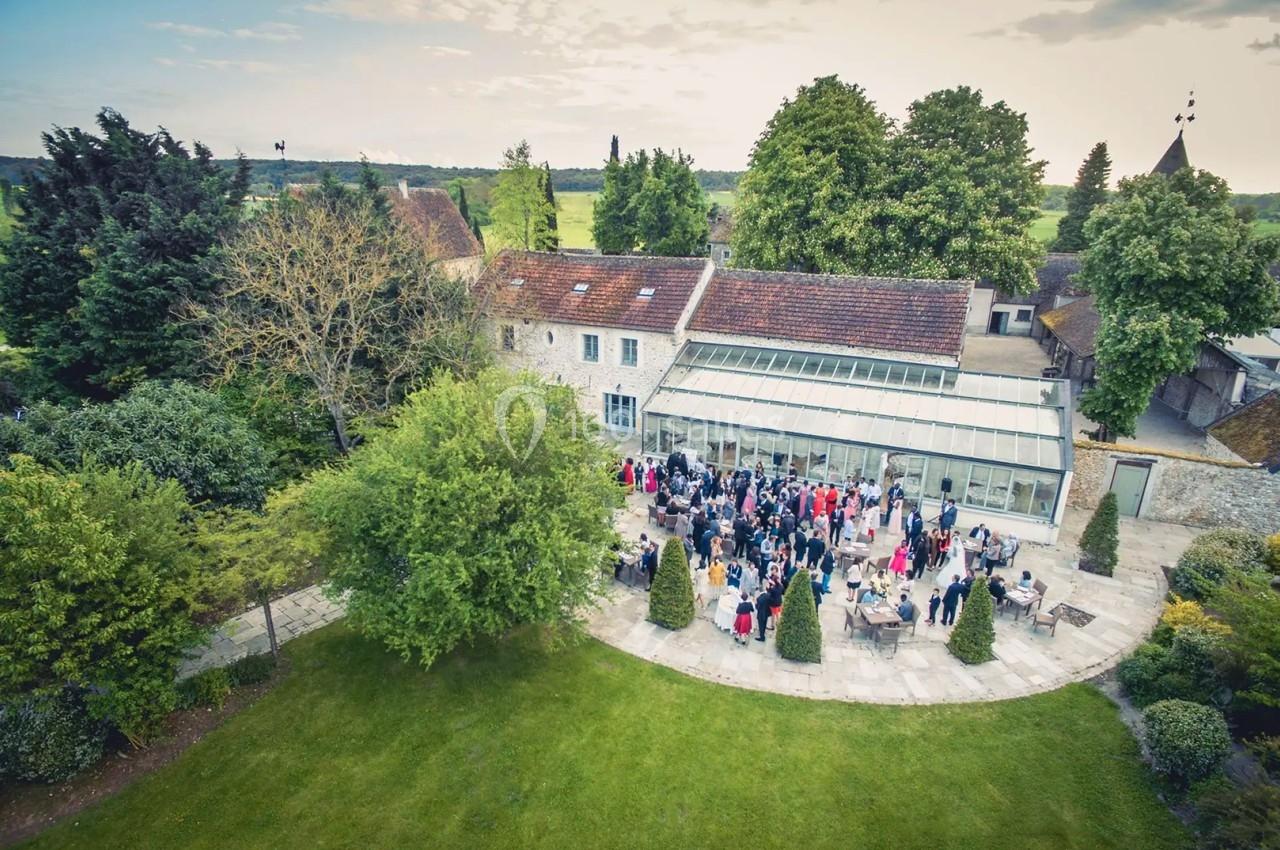 Vue aérienne d'un rassemblement de personnes dans une cour pavée entourée de verdure et d'un bâtiment en pierre.