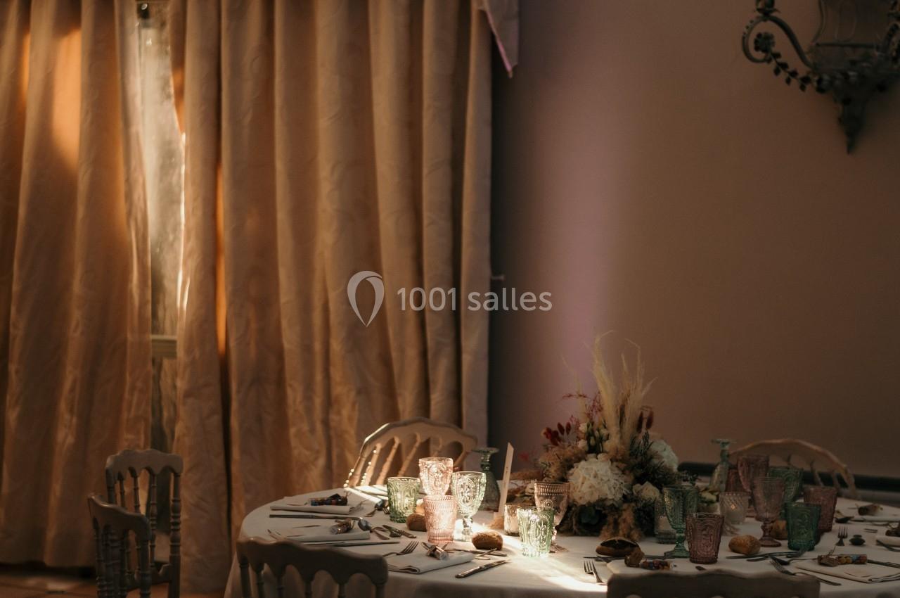 Table ronde élégamment dressée avec vaisselle raffinée, décorée de fleurs, sous un éclairage tamisé et un lustre.