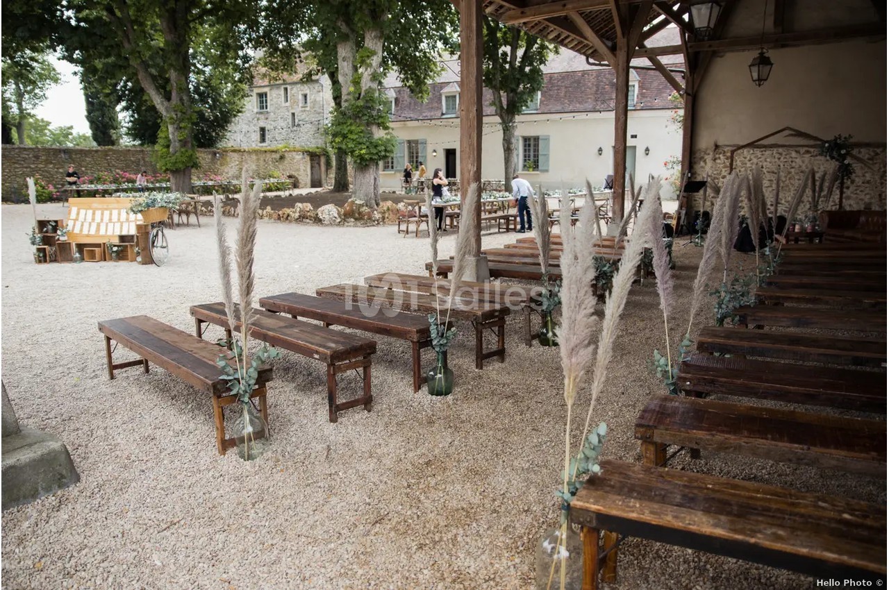 Bancs en bois disposés en rangées dans une cour extérieure avec décoration végétale et ambiance champêtre.