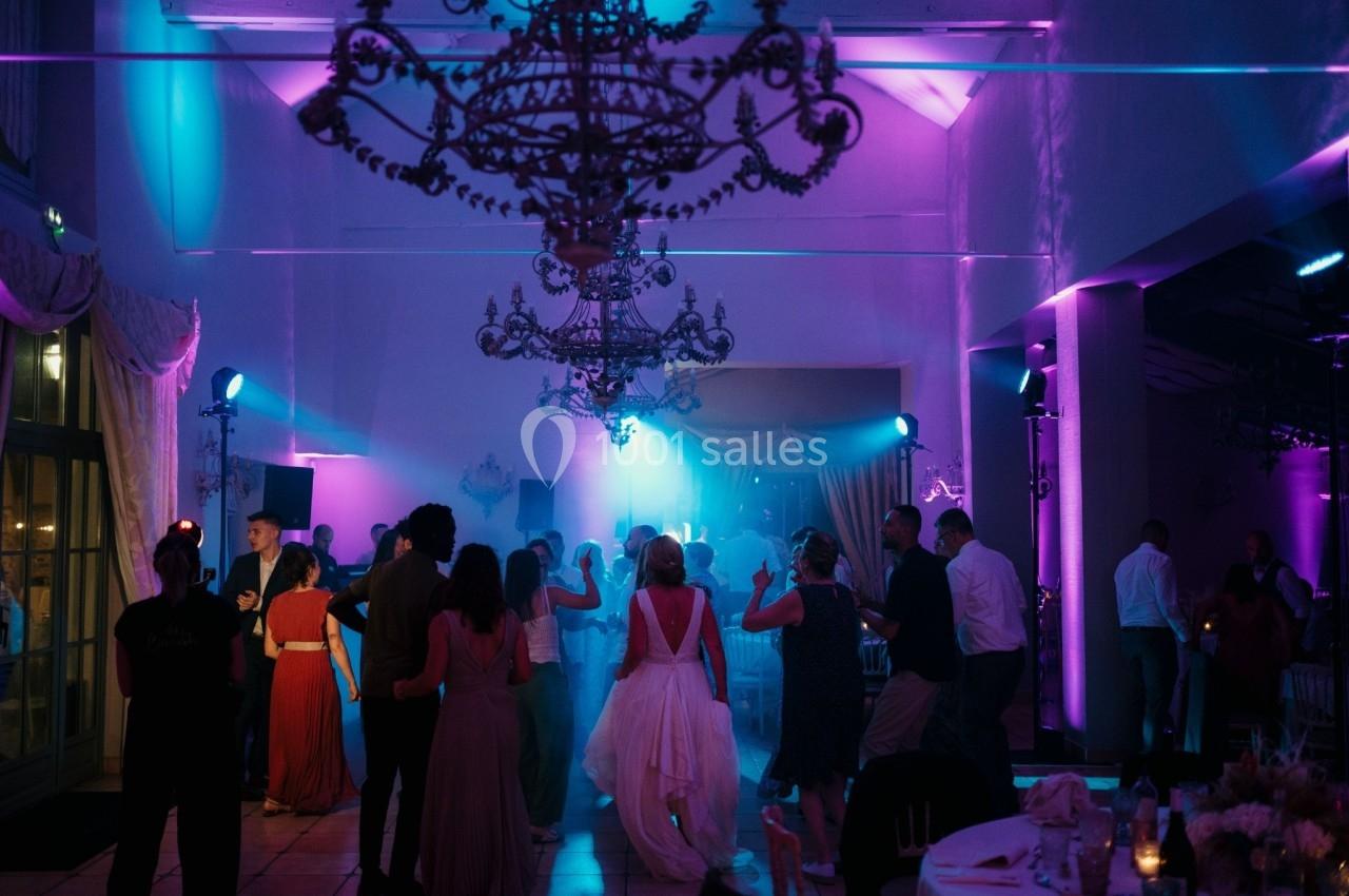 Des invités dansent sous des lumières colorées dans une salle de réception décorée de lustres.