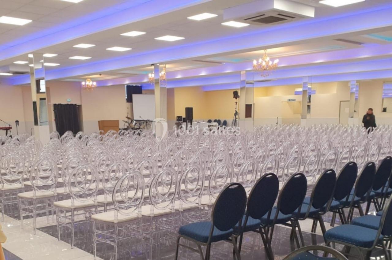 Salle de conférence lumineuse avec des rangées de chaises transparentes et bleues, équipée d'écrans et de matériel audio.