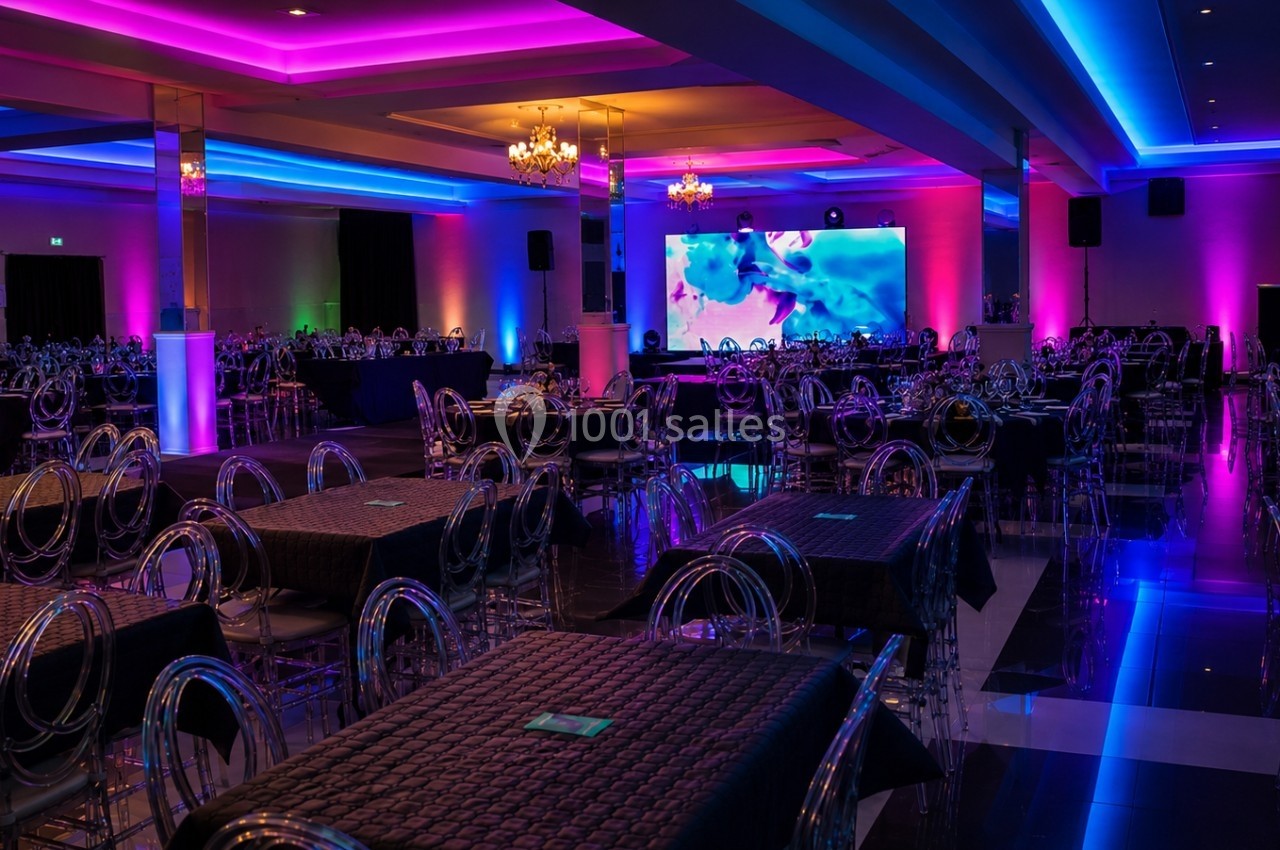 Salle de réception avec tables dressées, chaises transparentes et éclairage coloré violet et bleu.
