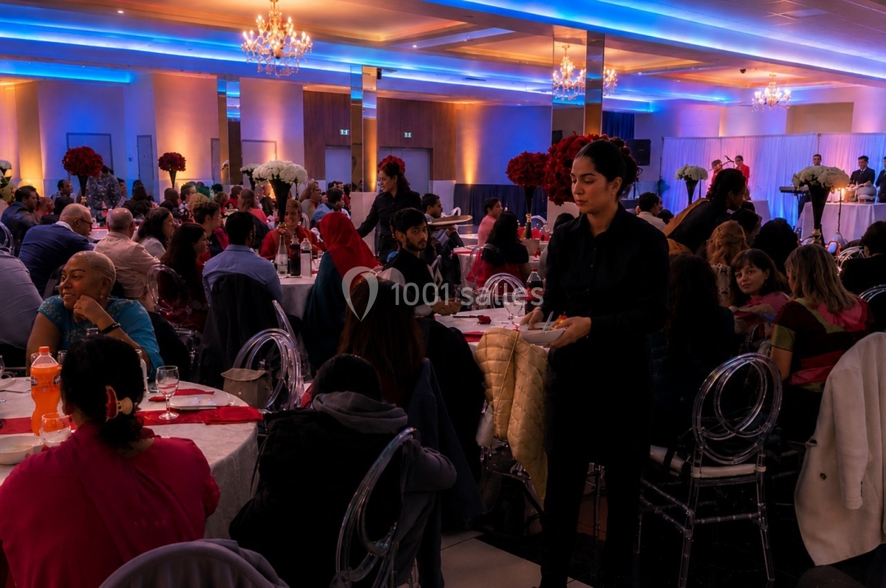 Salle de réception éclairée avec des invités assis à des tables décorées, et un serveur en train de circuler.