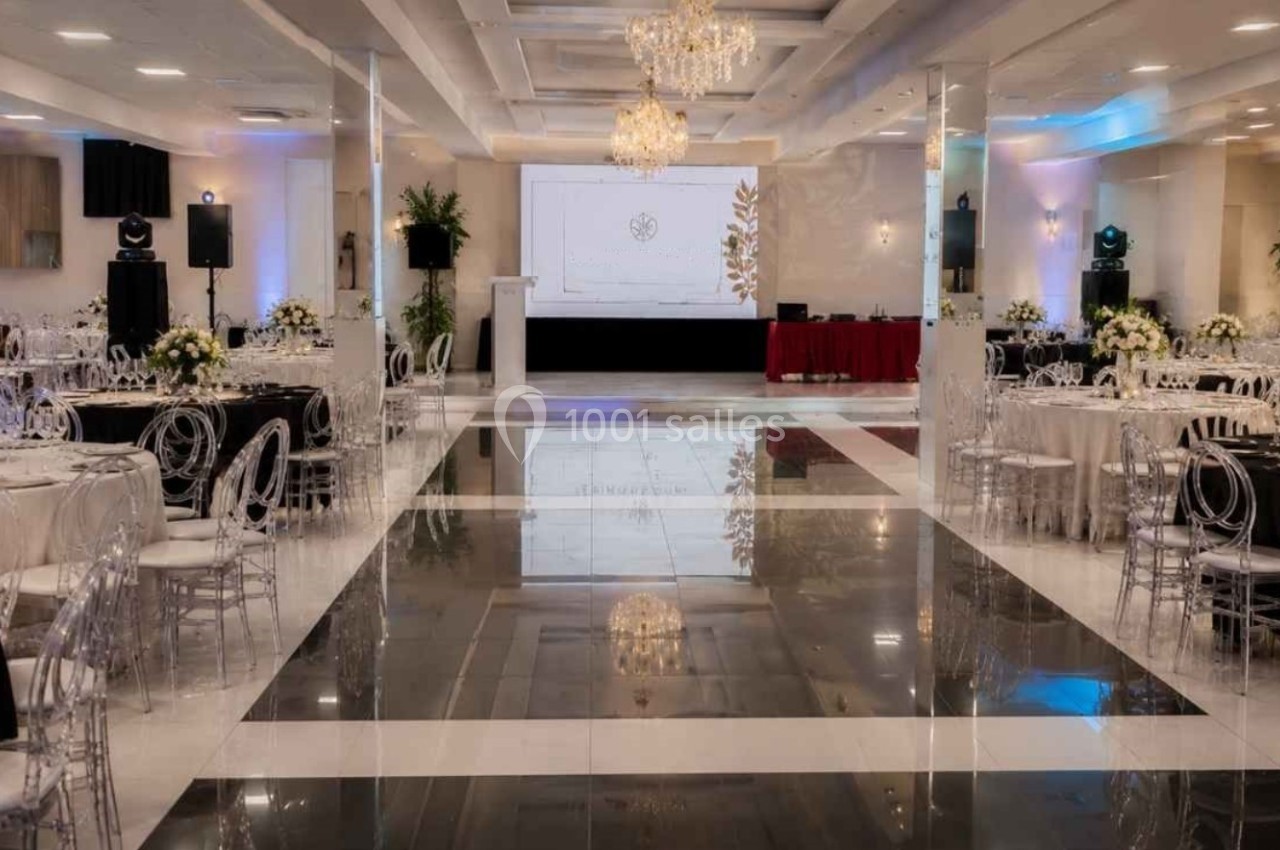 Salle de réception élégante avec tables dressées, chaises transparentes et lustres, prête pour un événement.