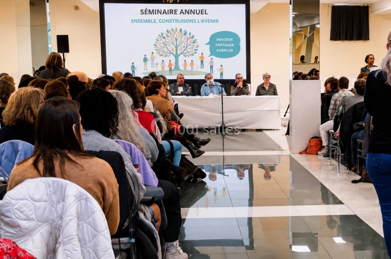 Salle comble lors d’un séminaire annuel, avec des intervenants assis sur une scène et un public attentif.