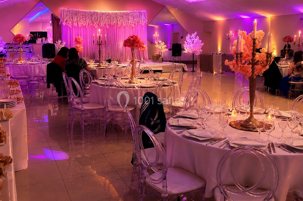 Salle de réception décorée avec des tables rondes, des chaises transparentes et des arrangements floraux colorés.