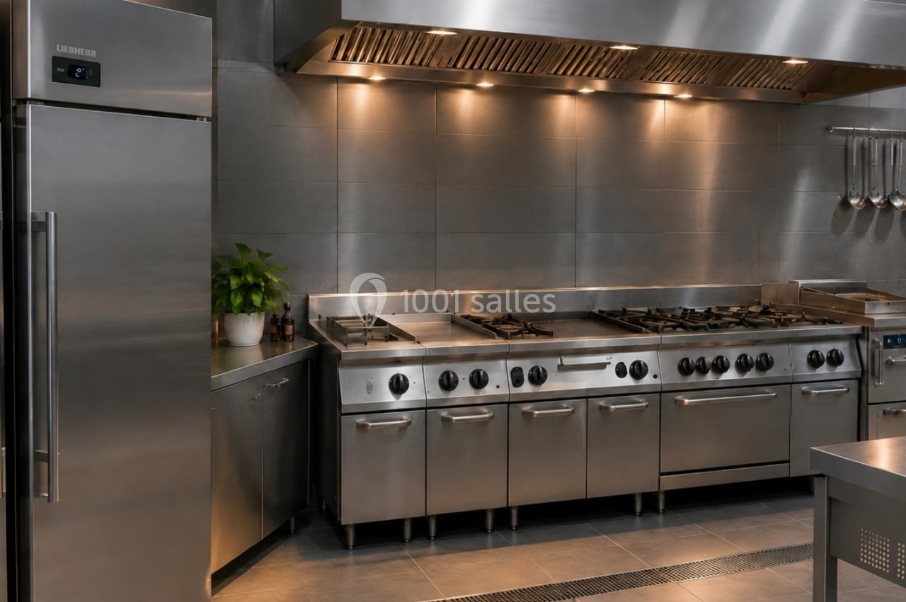 Cuisine professionnelle moderne avec équipements en acier inoxydable, réfrigérateurs, plaques de cuisson et hotte aspirante.