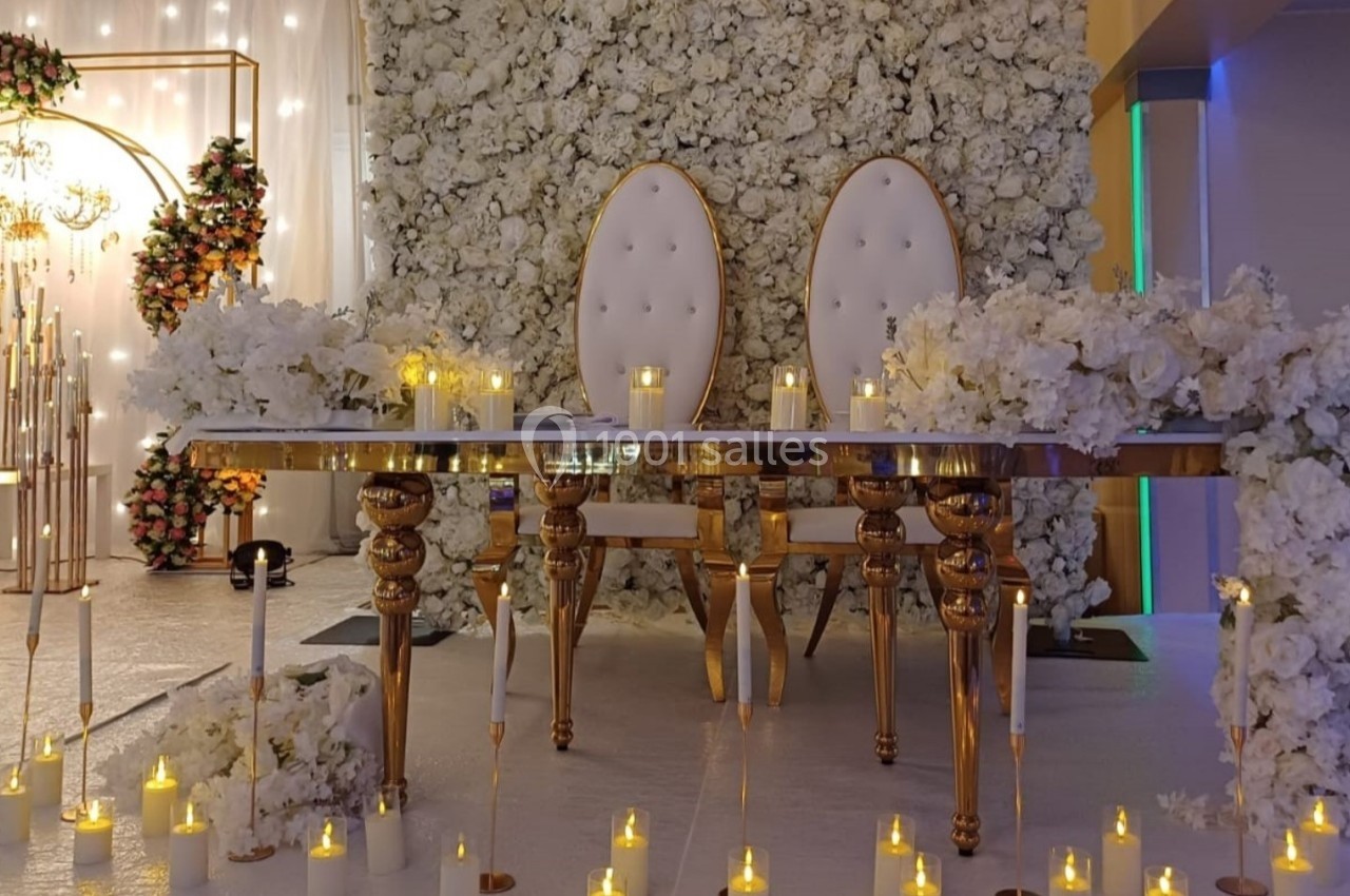 Deux chaises blanches capitonnées derrière une table décorée de fleurs blanches et de bougies, dans un décor de mariage.