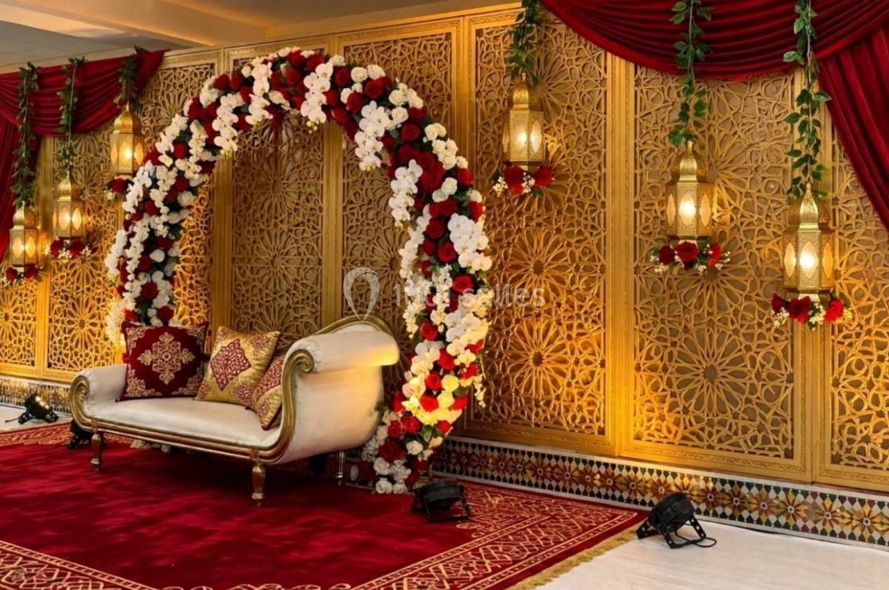 Décor de cérémonie avec arche florale rouge et blanche, canapé doré, lanternes suspendues et rideaux rouges.