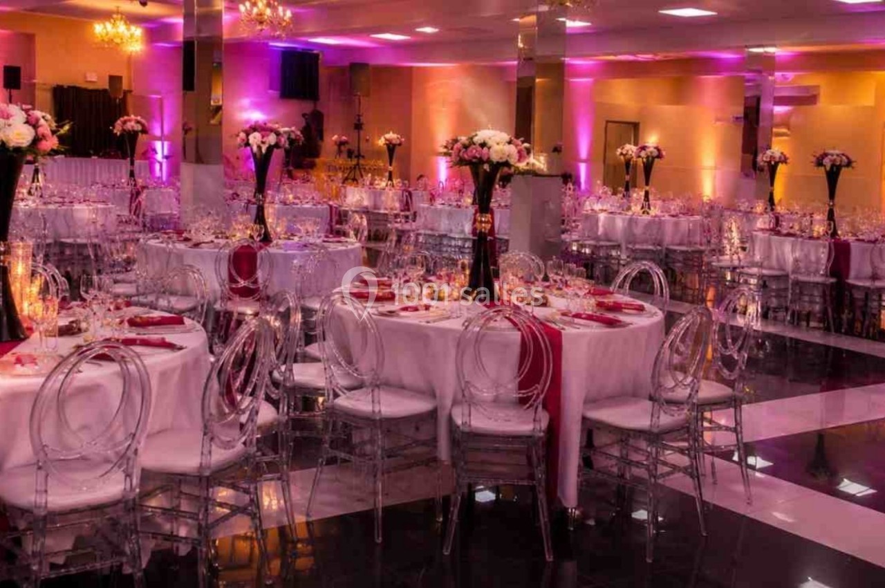Salle de réception décorée avec des tables rondes, nappes blanches, chaises transparentes et éclairage rose.