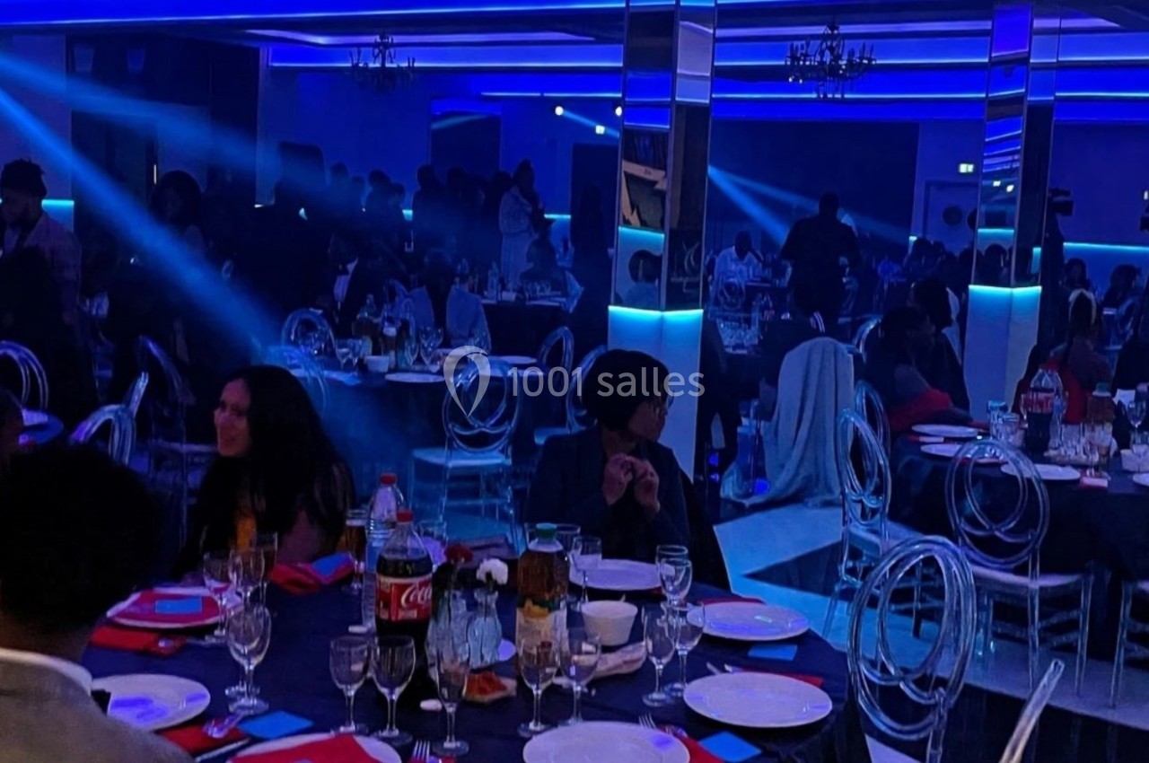 Salle de réception avec invités assis à des tables dressées, éclairage bleu et ambiance festive.