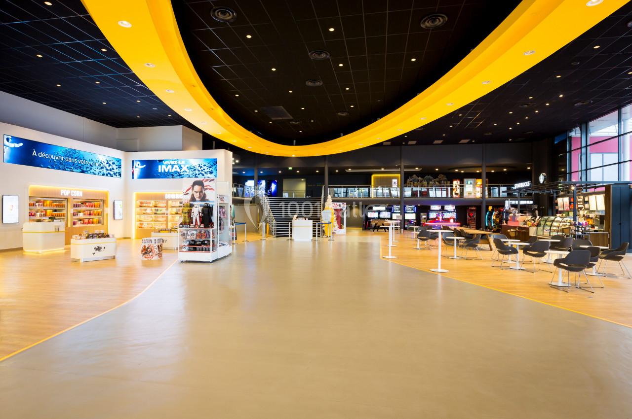 Hall spacieux d'un cinéma avec comptoirs, affiches, sièges et éclairage moderne sous un plafond noir et jaune.