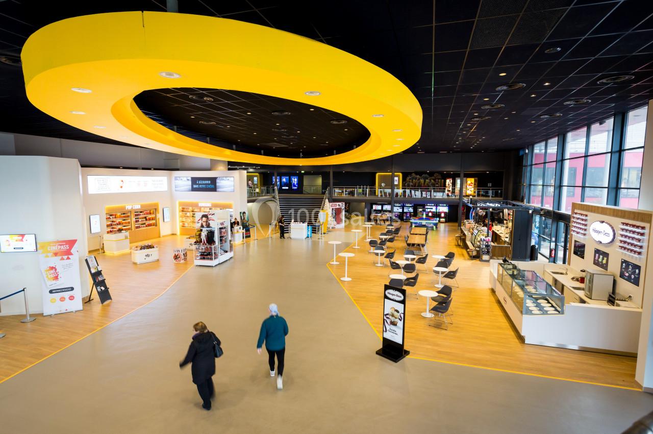 Vue intérieure d'un espace moderne avec comptoirs, tables, vitrines et un grand anneau jaune suspendu au plafond.