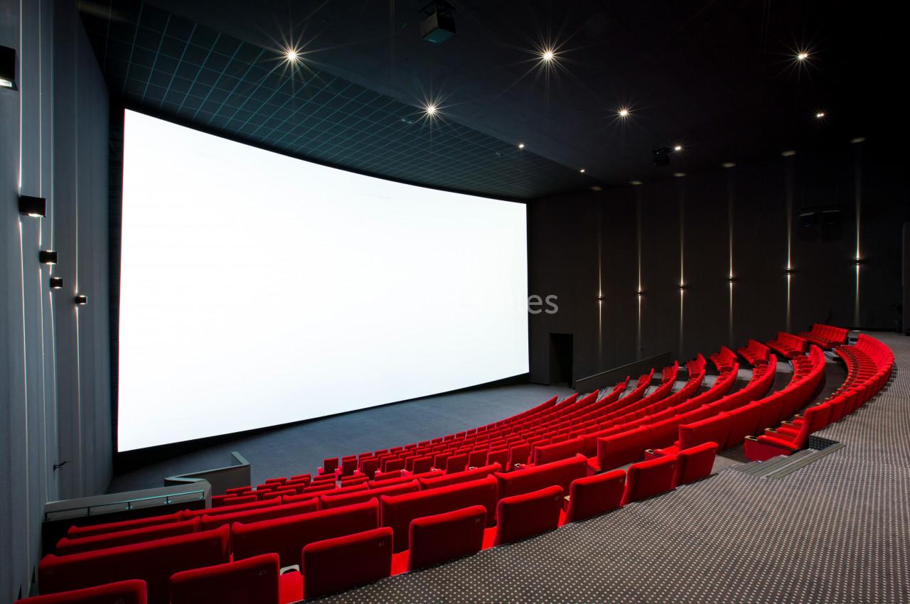 Salle de cinéma moderne avec des rangées de sièges rouges et un grand écran blanc allumé.