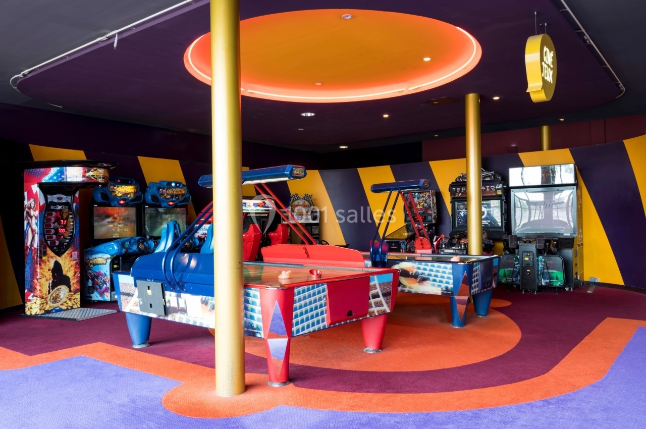 Location salle Dammarie-les-Lys (Seine-et-Marne) - Pathé Dammarie #6 Salle d'arcade colorée avec des machines de jeux, des tables de hockey sur air et un éclairage néon au plafond.