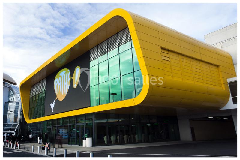 Façade moderne d'un cinéma avec structure jaune incurvée et écran numérique affichant un logo coloré.