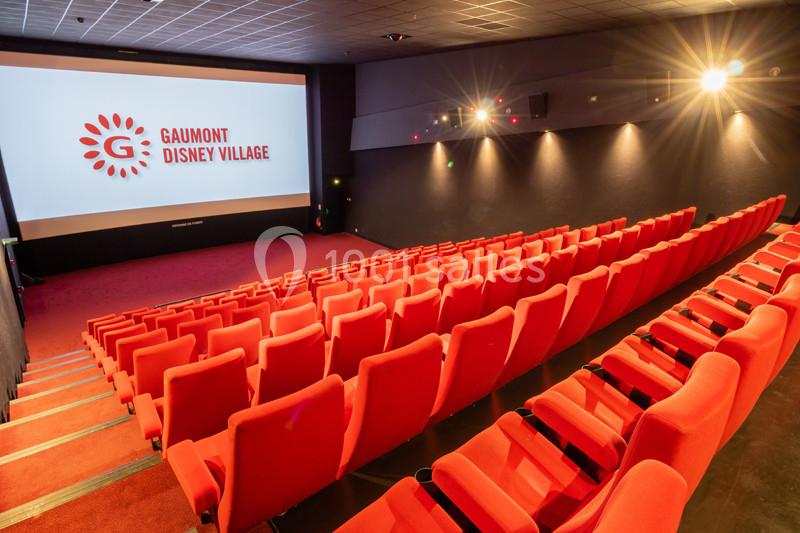 Salle de cinéma vide avec rangées de sièges rouges et écran affichant ’Gaumont Disney Village’.