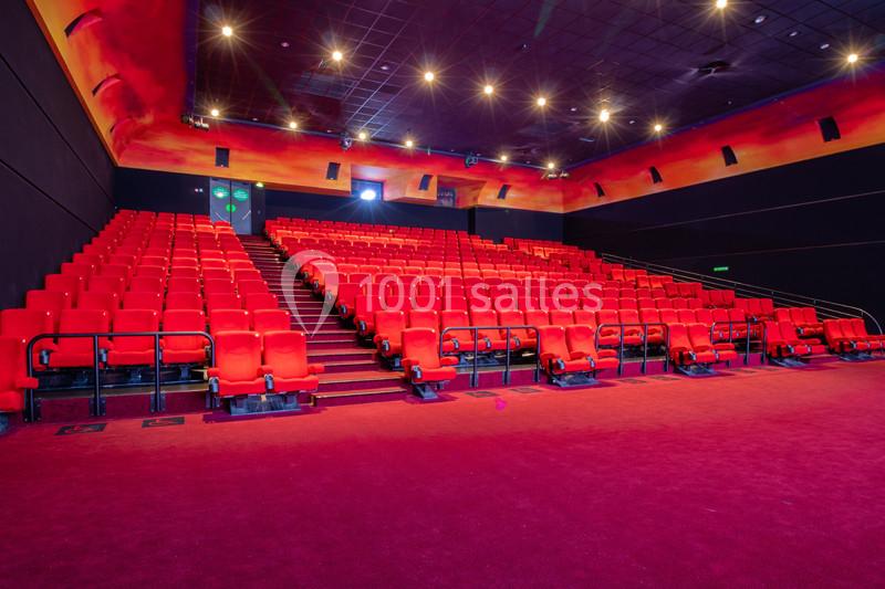 Salle de cinéma vide avec des rangées de sièges rouges et un éclairage tamisé.