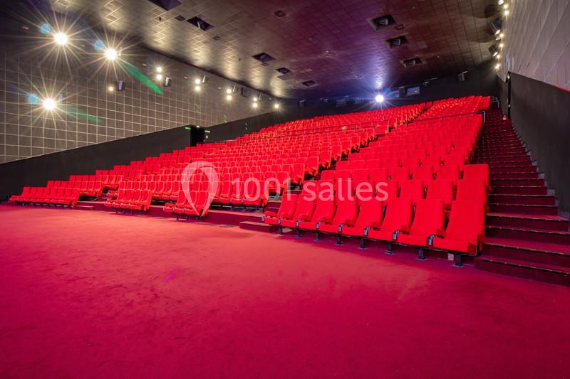 Salle de cinéma vide avec des rangées de fauteuils rouges et un sol recouvert de moquette rouge.
