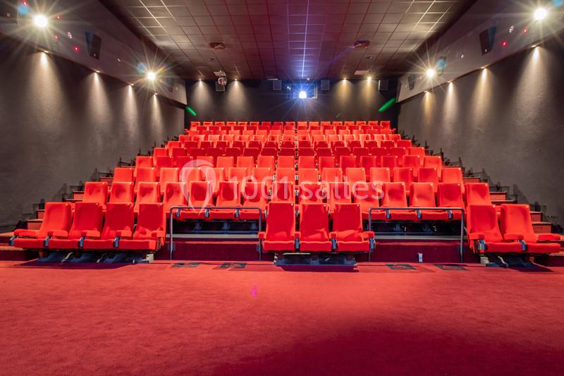 Salle de cinéma vide avec des rangées de sièges rouges, éclairage tamisé et écran en fond.
