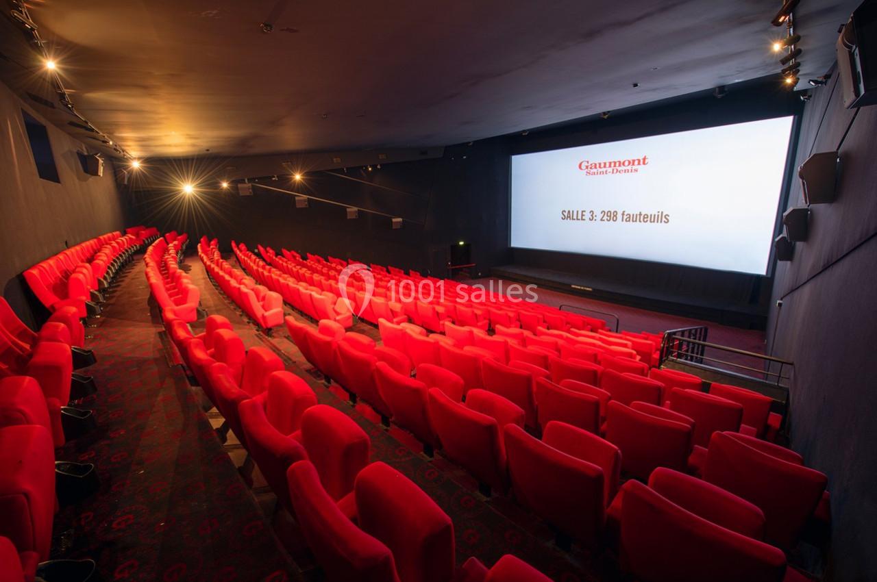 Salle de cinéma avec rangées de fauteuils rouges vides et écran affichant des informations sur la capacité.