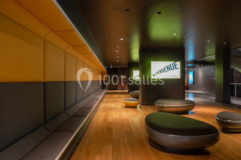 Un hall moderne avec des bancs rembourrés, des poufs ovales et des panneaux lumineux affichant ’Bienvenue’.