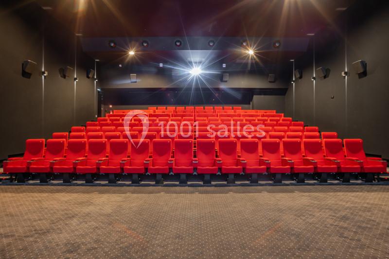 Salle de cinéma vide avec des rangées de sièges rouges et un écran hors champ à l'avant.