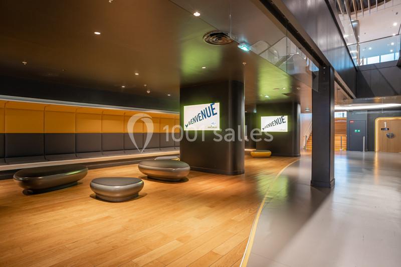 Espace intérieur moderne avec bancs arrondis, panneaux ’Bienvenue’ lumineux et murs aux tons jaunes et gris.