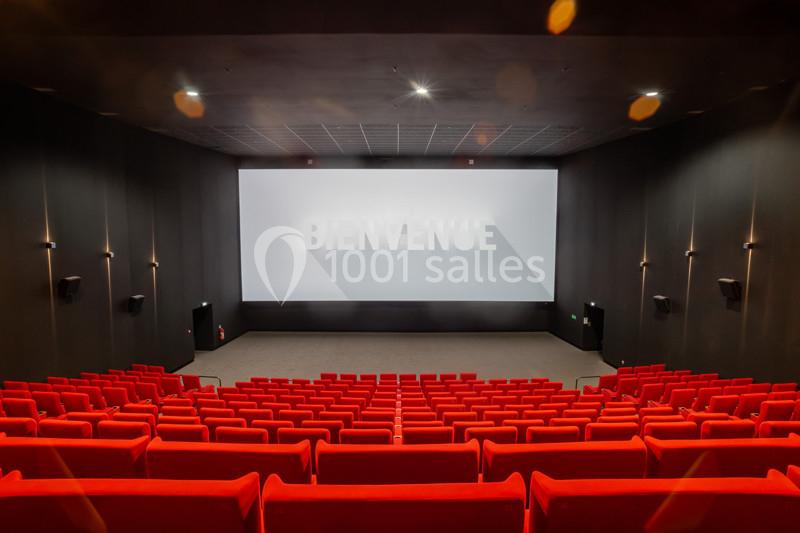 Salle de cinéma vide avec des rangées de sièges rouges et un écran affichant le mot ’Bienvenue’.