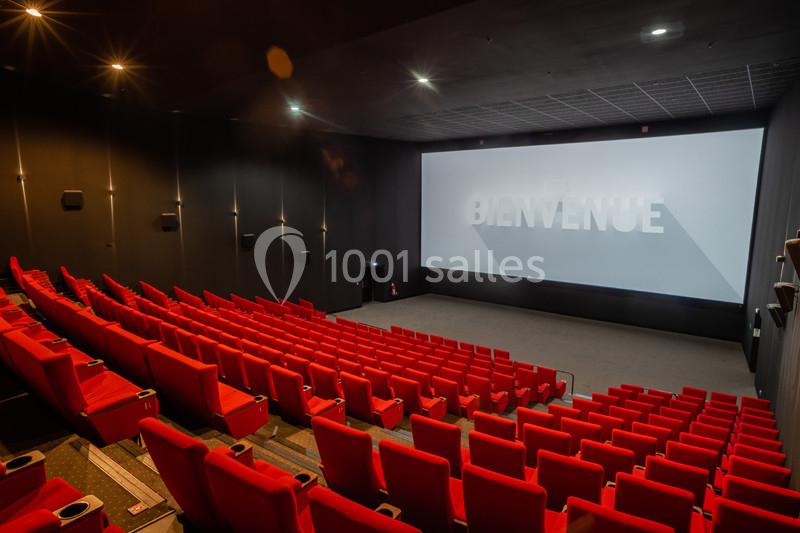Salle de cinéma vide avec des sièges rouges, un grand écran affichant ’Bienvenue’ et un éclairage tamisé.