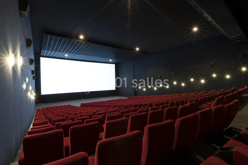 Location salle Ivry-sur-Seine (Val-de-Marne) - Pathé Quai D'ivry #3 Salle de cinéma vide avec rangées de sièges rouges et un grand écran blanc allumé.