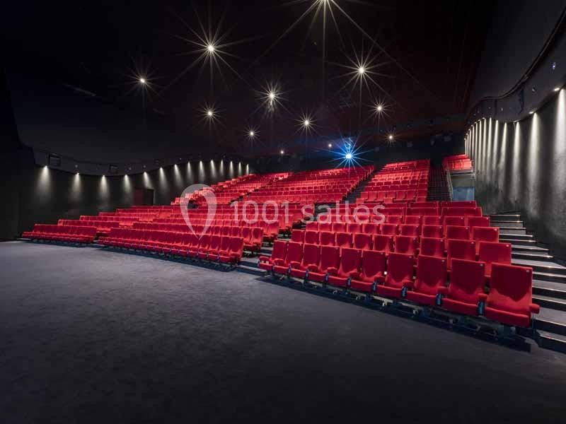 Salle de cinéma vide avec des rangées de sièges rouges et un éclairage tamisé.