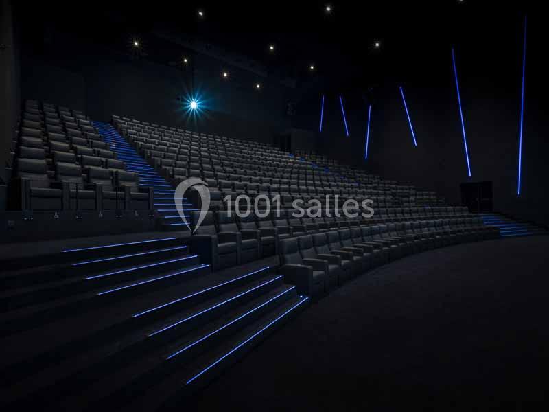 Salle de cinéma vide avec sièges en gradins, éclairage tamisé et bandes lumineuses bleues sur les marches.