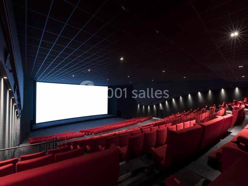 Salle de cinéma vide avec des rangées de fauteuils rouges et un grand écran blanc allumé.