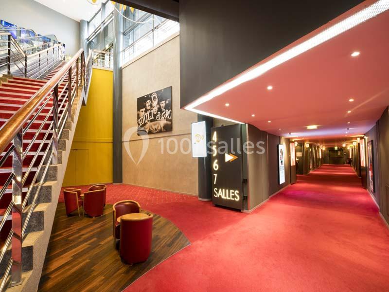 Location salle Boulogne-Billancourt (Hauts-de-Seine) - Pathé Boulogne #12 Hall de cinéma avec escalier, fauteuils rouges, affiches murales et couloir menant aux salles numérotées.