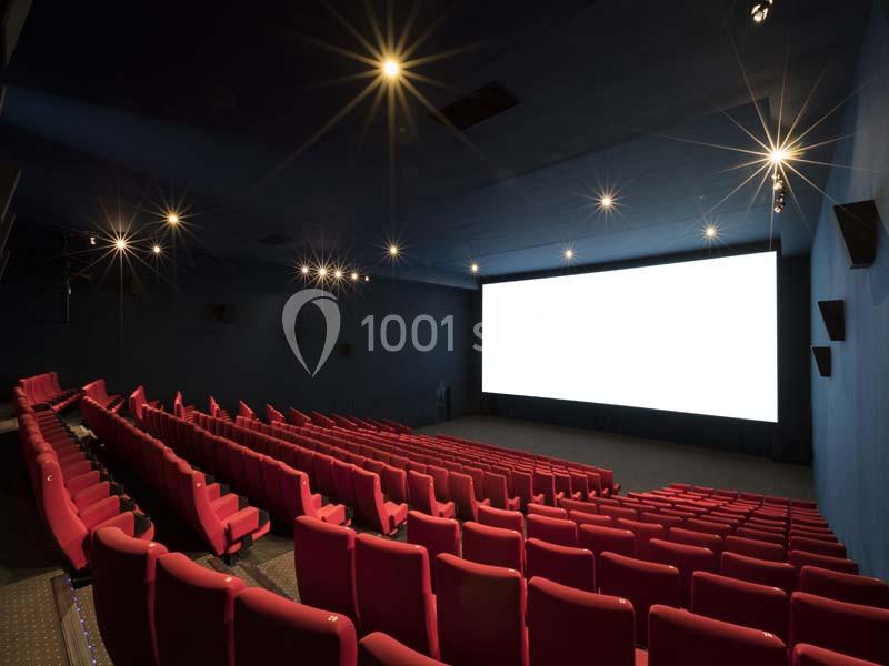 Location salle Boulogne-Billancourt (Hauts-de-Seine) - Pathé Boulogne #3 Salle de cinéma vide avec des rangées de sièges rouges et un grand écran blanc allumé.