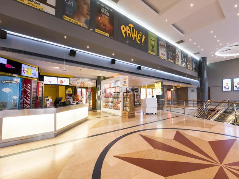 Location salle Boulogne-Billancourt (Hauts-de-Seine) - Pathé Boulogne #14 Hall d'entrée lumineux d'un cinéma avec comptoirs de vente, affiches de films et sol en marbre décoratif.