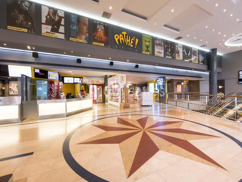 Location salle Boulogne-Billancourt (Hauts-de-Seine) - Pathé Boulogne #1 Hall d'entrée d'un cinéma avec comptoirs de billetterie, affiches de films et décoration au sol en étoile.
